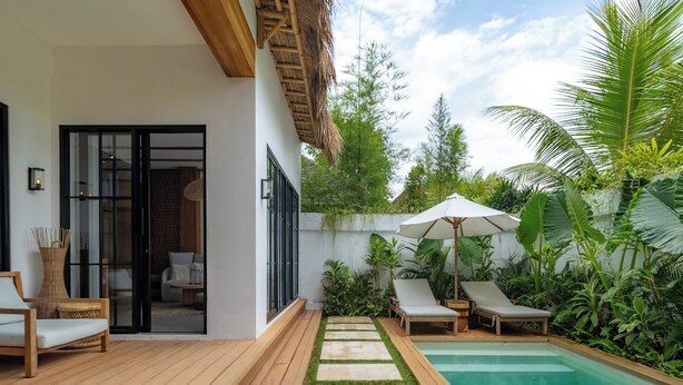 A modern outdoor pool area with a wooden deck, lounge chairs, and a glass door entrance. - Como Villa by Betterplace (Ubud)