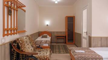 Une chambre avec deux lits, un fauteuil roulant, un miroir et une armoire en bois.