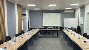 A conference room with a long table, chairs, a projector screen, and a whiteboard.