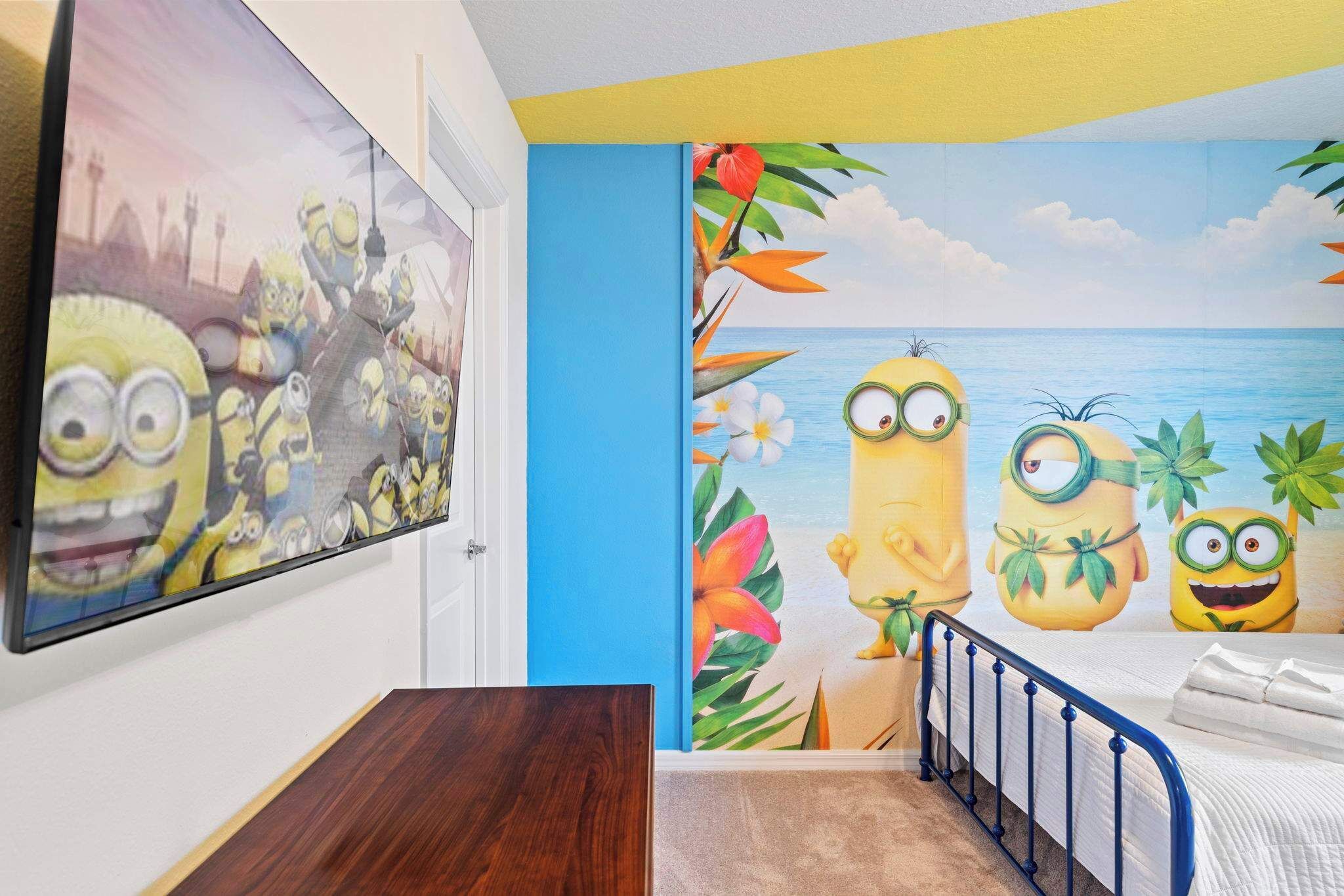 Une chambre avec une fresque murale représentant les Minions sur une plage, un lit et une table de chevet.