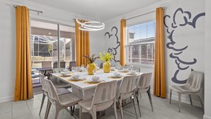 A dining area with a table set for four, chairs, a vase with flowers, and a wall with a large abstract design.