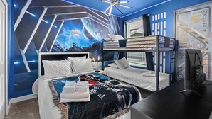 A bedroom with a bunk bed, a desk, and a large mural of space on the wall.