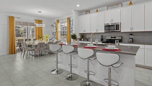 A modern kitchen with white cabinets, a stainless steel microwave, and a bar area with stools.