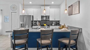 A modern kitchen with white cabinets, a central island with bar stools, and pendant lighting. - Gorgeous 5bed TH close to Disney, Water Park (Davenport)