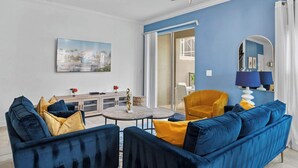A living room with a blue sofa, yellow cushions, a round coffee table, and a painting on the wall. - Gorgeous 5bed TH close to Disney, Water Park (Davenport)