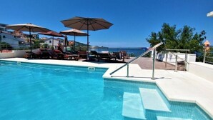 A pool with lounge chairs and umbrellas, overlooking a coastal area.