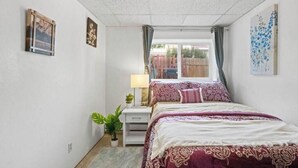 Un dormitorio con cama, mesita de noche, lámpara, planta en maceta y obras de arte en las paredes.