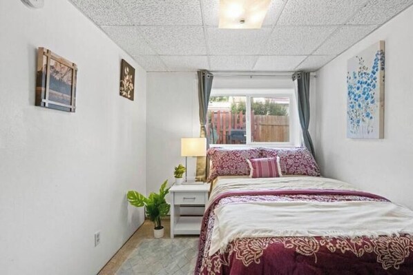 A bedroom with a bed, a nightstand, a lamp, a potted plant, and artwork on the walls.