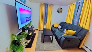 Una sala de estar con un televisor de pantalla plana, un sofá, una mesa de centro y cortinas amarillas.