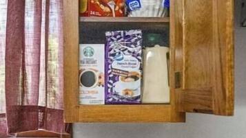 A kitchen with a coffee maker, a cabinet with food items, and a stove.