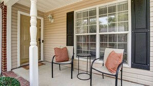 A porch with two chairs and a small table, a white door, and a window with shutters. - Cozy Bungalow in Wingate w Patio, Grill, Firepit - Easy Access To Bypass & Monroe! +15% Off Stay! (Wingate)