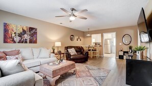 A living room with a sofa, coffee table, and a ceiling fan. There is a dining area with chairs and a table, and a kitchen with cabinets and appliances. - Cozy Bungalow in Wingate w Patio, Grill, Firepit - Easy Access To Bypass & Monroe! +15% Off Stay! (Wingate)