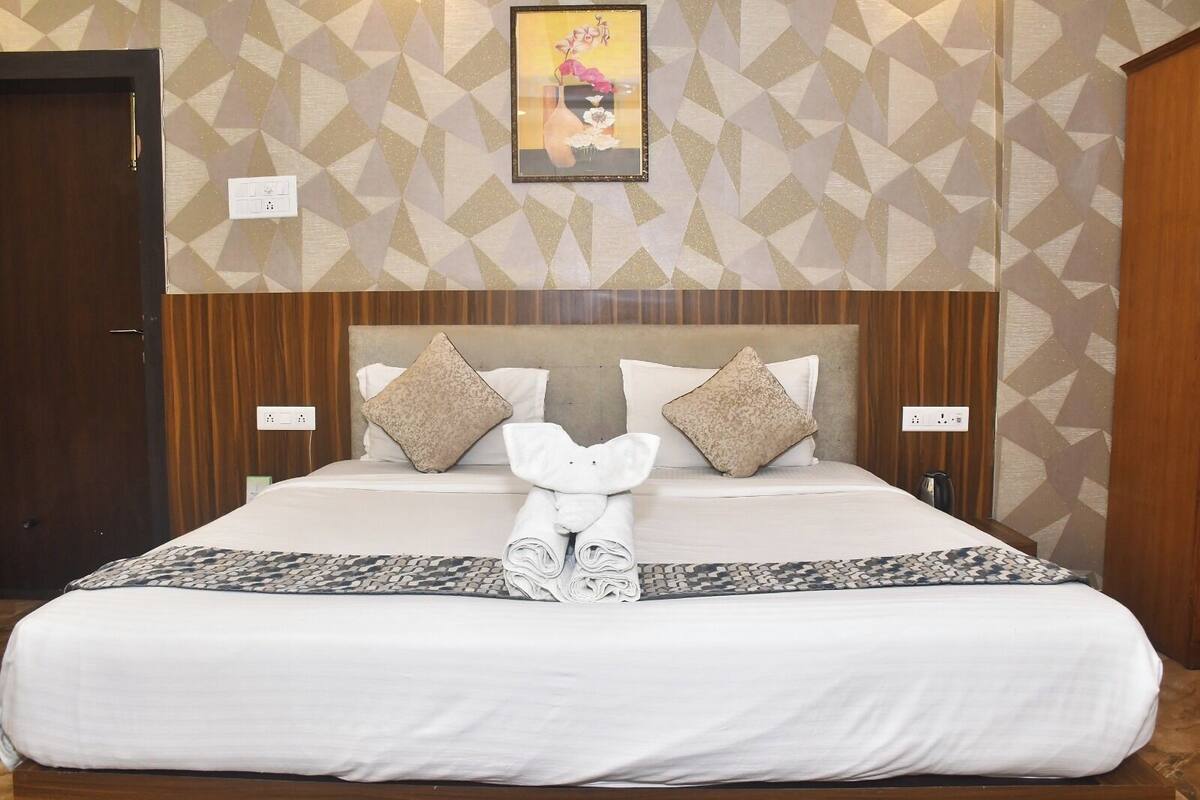A hotel room with a large bed, two pillows, a framed picture on the wall, and a towel rack.