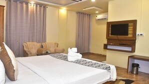 Een hotelkamer met een groot bed, twee fauteuils, een televisie en een airconditioner.