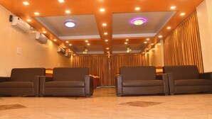 Een hotellobby met een rij zwarte leren stoelen, een plafond met inbouwspots en een luchtverwarmer aan de muur.