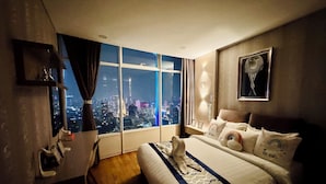 Une chambre d’hôtel dotée d’une grande fenêtre donnant sur la ville, d’un lit recouvert d’une couvre-lit à motifs et d’une table de chevet avec une lampe.