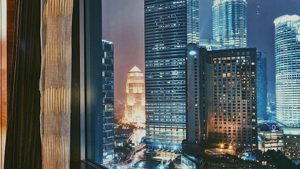 Vue des tours jumelles Petronas la nuit, prise à travers une fenêtre avec un rideau.