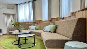 A modern living room with a sectional sofa, two round tables, a green rug, and a large window with curtains. - ADVENTURe (Furano)