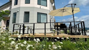 A modern multi-story building with a balcony, outdoor seating, and a large umbrella. - ADVENTURe (Furano)