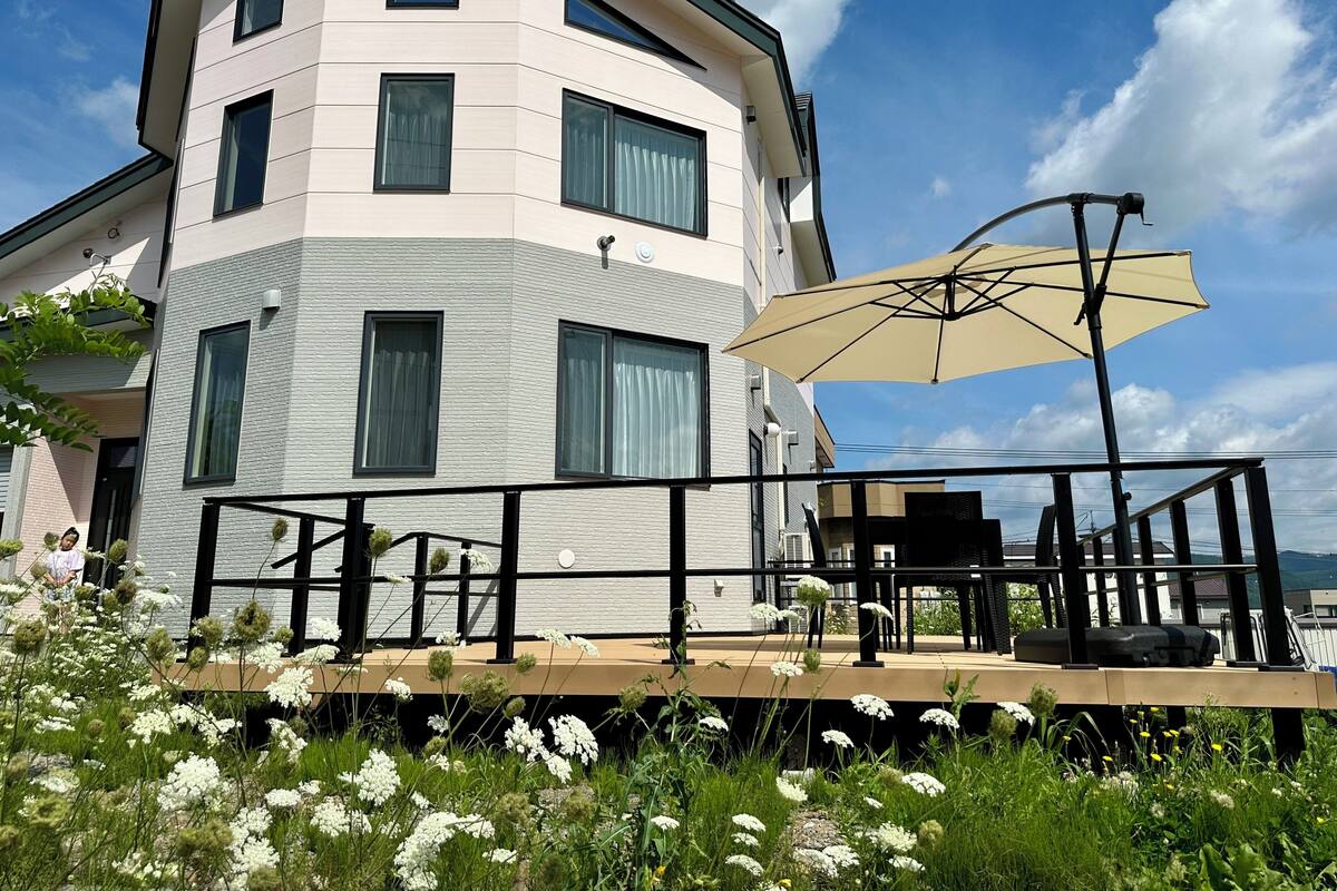 Ein modernes Mehrstöckengebäude mit Balkon, Sitzgelegenheiten im Freien und einem großen Sonnenschirm.
