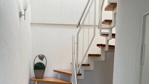 Eine Treppe mit Holzsitzstufen und einem Metallgeländer, die zu einer Zwischenebene mit weißer Wand und einer wandmontierten Leuchte führt.