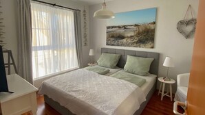 Ein Schlafzimmer mit einem Bett, einem Schreibtisch, einem Stuhl, einer Lampe und einem Bild an der Wand.