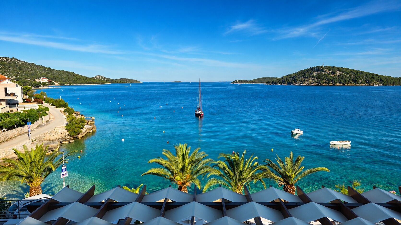 A coastal view with a clear blue sea, a sailboat, and a small boat.