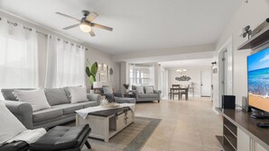A spacious living room with a grey sofa, a coffee table, and a TV on a wooden stand. - Updated! Beachside Bi-level Unit, Sleeps 10! FREE Activities! Pool, FREE Parking ~ C400 Sun & Sea (Indian Rocks Beach)
