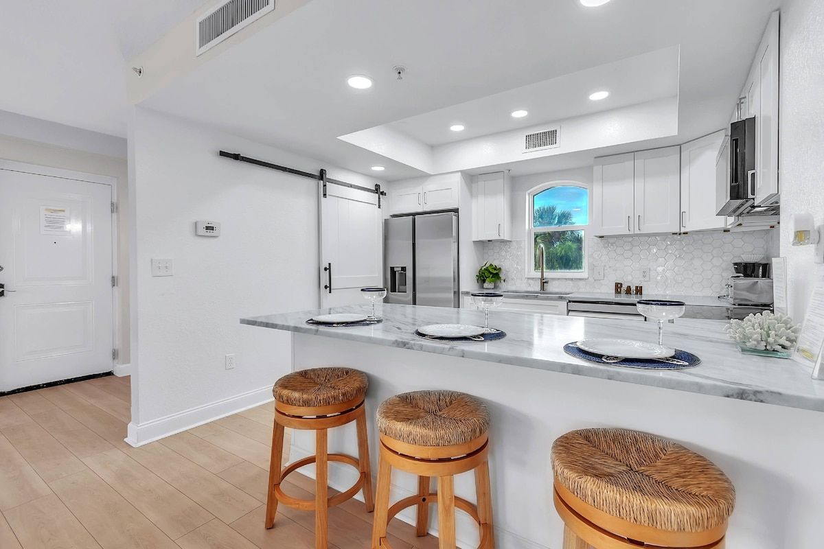 A modern kitchen with white cabinetry, a central island with stools, and a view of the outdoors.
