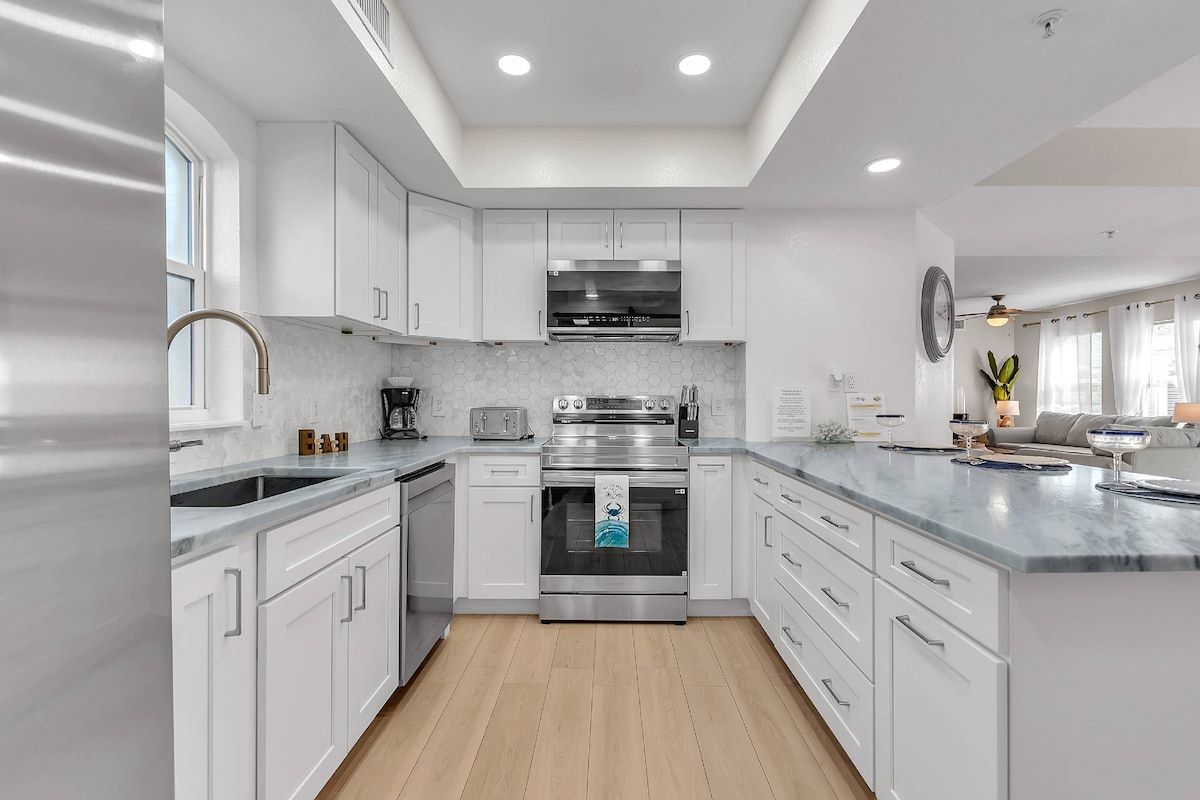 Una cocina moderna con armarios blancos, electrodomésticos de acero inoxidable y suelo de madera.