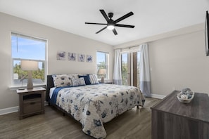 A bedroom with a bed, bedside tables, a ceiling fan, and a view of the outdoors.