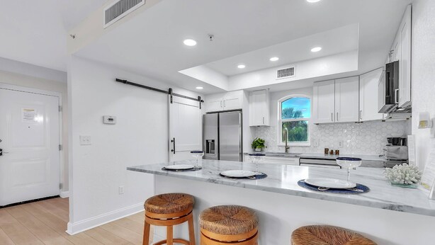 A modern kitchen with white cabinets, a large island with stools, and a view of the outdoors. - Updated! Beachside Bi-level Unit, Sleeps 10! FREE Activities! Pool, FREE Parking ~ C400 Sun & Sea (Indian Rocks Beach)