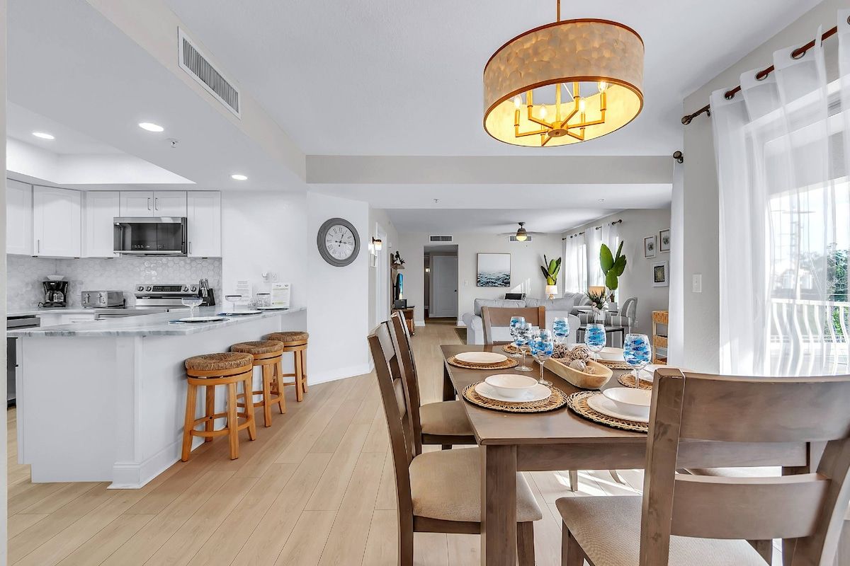 Cozinha moderna com ilha central, banquetas de madeira e área de refeições com mesa posta para quatro pessoas.
