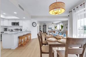 Een moderne keuken met een centraal eiland, houten barkrukken en een eethoek met een tafel voor vier personen.