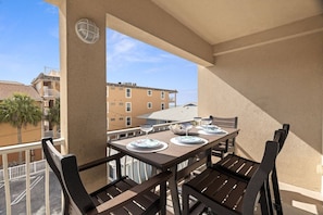 Un balcón con una mesa lista para cuatro personas, sillas y vistas a edificios al fondo.