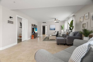 A spacious living room with a grey sofa, a television, and a ceiling fan.