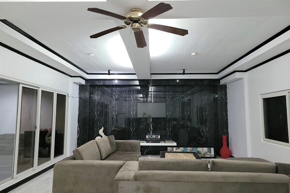 Una sala de estar moderna con un sofá seccional, un ventilador de techo, un televisor de pantalla plana y una pared de acento de mármol.