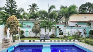 A swimming pool with blue tiles, surrounded by a garden with palm trees and a white wall with a statue. - Jewelry Resort and Villas Tagaytay (Silang)