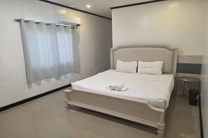 A bedroom with a bed, a window with curtains, a bedside table, and a trash bin. - Jewelry Resort and Villas Tagaytay (Silang)