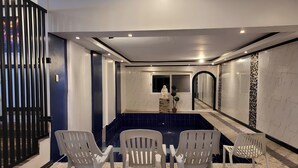 A modern bathroom with a large mirror, a small sink, and a blue-tiled floor. There are four white plastic chairs arranged around a small pool. - Jewelry Resort and Villas Tagaytay (Silang)