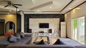 A modern living room with a sofa, a coffee table with a plant, a flat-screen TV mounted on the wall, and a patterned floor. - Jewelry Resort and Villas Tagaytay (Silang)