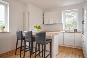 Een moderne keuken met witte kastjes, een houten aanrecht en twee zwarte barkrukken.