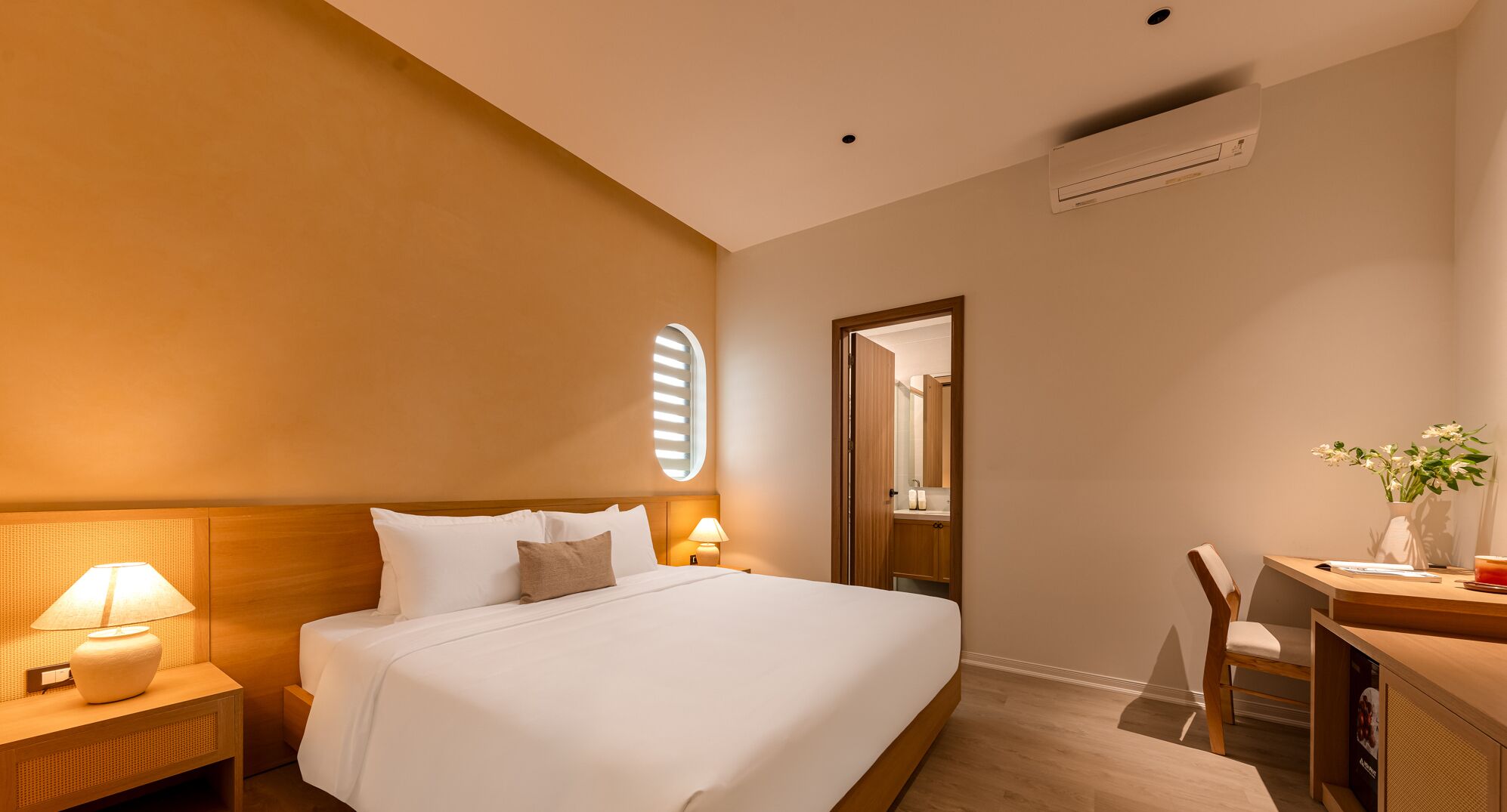 A hotel room with a large bed, bedside lamps, a desk with a chair, and a mirror.