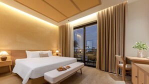 Une chambre d’hôtel moderne dotée d’un grand lit, de lampes de chevet, d’une banquette, d’un bureau et offrant une vue sur le paysage urbain grâce à de grandes fenêtres du sol au plafond.