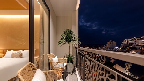 Un balcon avec un lit, des fauteuils en osier et une plante en pot.