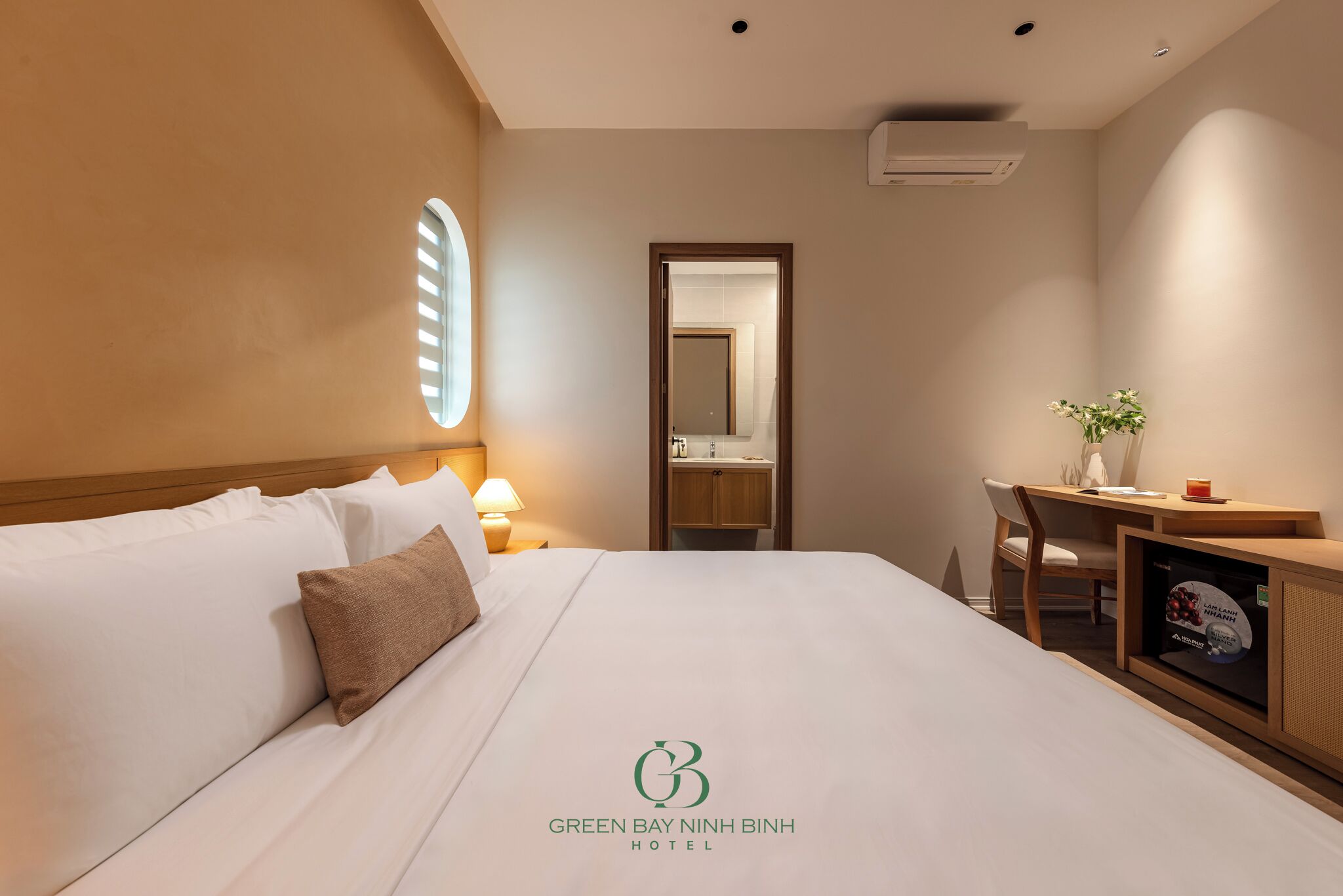 Habitación de hotel con cama, escritorio, silla, espejo y una planta pequeña.
