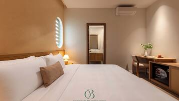 Habitación de hotel con cama, escritorio, silla, espejo y una planta pequeña.