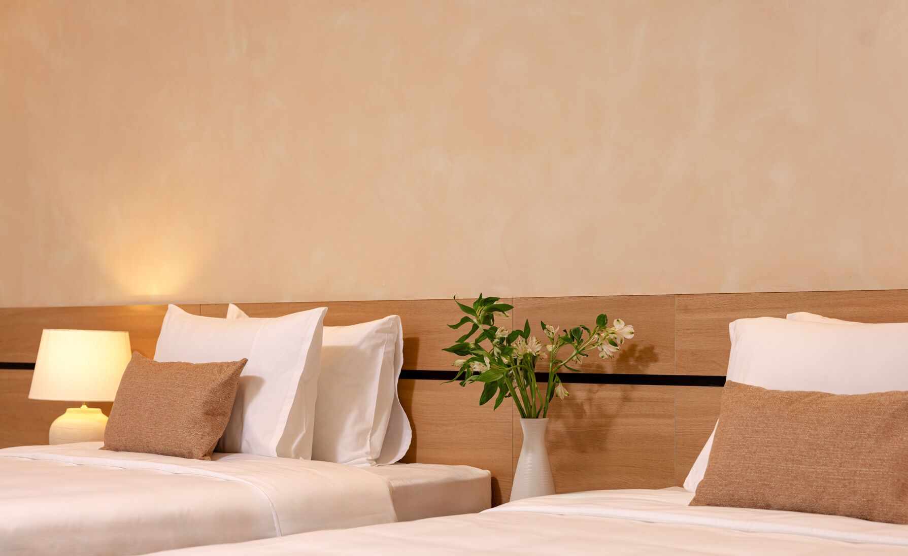 A hotel room with two beds, a nightstand with a lamp, and a vase with flowers.