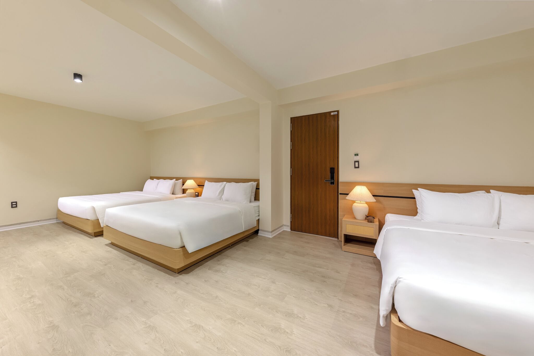 Une chambre d’hôtel avec trois lits, des têtes de lit en bois et des lampes de chevet.