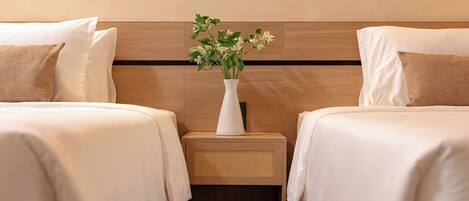 Habitación de hotel con dos camas, una mesita de noche con un jarrón de flores y un logotipo en la mesita.